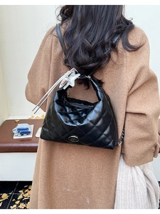 Close-up of black quilted leather tote bag with star charm worn on a brown wool coat