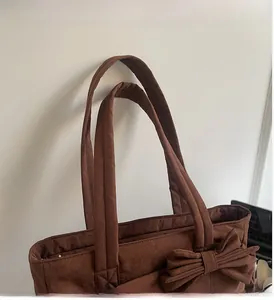 Detail view of durable brown tote bag handles and a large decorative nylon bow