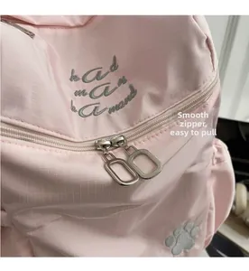 Close-up of smooth silver zippers and cat paw embroidery on pink plaid fabric backpack