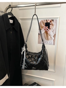Detail of black quilted hobo bag with metal logo plate and decorative chain tassels