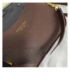 Close-up of dark brown leather shoulder bag with gold brand logo and metal chain details