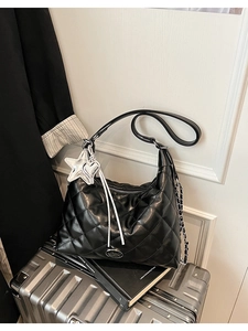 Detail of black quilted hobo bag with silver star charms on a silver suitcase