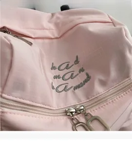 Detailed close-up of pink ripstop nylon backpack with embroidery and metal zippers
