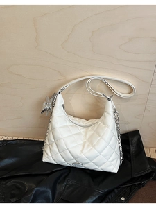 Close-up of white quilted hobo bag with star charm and silver chain on leather background
