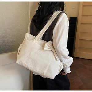 Vue latérale du grand sac cabas crème avec nœud porté à l'épaule dans un décor d'intérieur