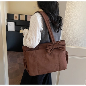 Détail du grand sac cabas marron montrant le nœud décoratif et la poche latérale pratique