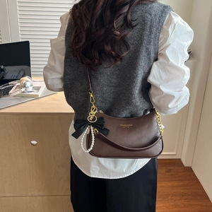 Detail of dark brown lychee leather bag with gold chain and pearl bow charm accessory