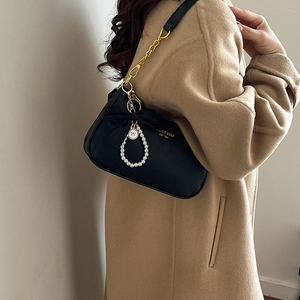 Detail of black textured leather bag with gold logo, pearl bow charm and chain strap