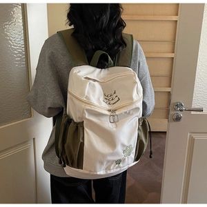 Detail of a beige and olive green backpack featuring artistic embroidery and side drawstring pocket