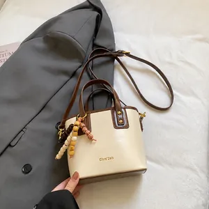 Vue détaillée du sac seau contrasté avec pendentif en perles de bois sur veste grise
