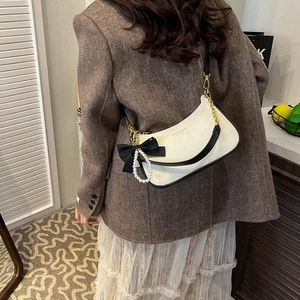 Detail of white lychee texture shoulder bag with black bow and pearl pendant on model