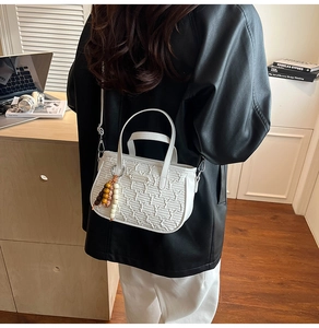 Sac bandoulière blanc à texture matelassée et breloque en bois sur une veste en cuir