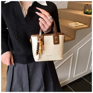 Detail of cream and brown bucket bag with gold lettering and decorative wooden bead charm