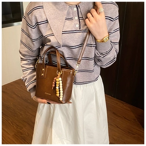 Détail d'un sac seau marron en cuir avec pompon en perles de bois et logo en relief
