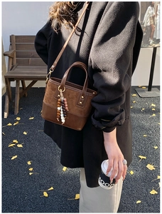 Gros plan sur un sac seau en daim marron avec breloque vintage dans un décor d'automne