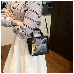Détail du sac seau vintage noir avec breloque en perles de bois et logo de marque
