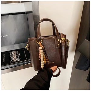 Detail view of dark brown bucket bag with shiny faux leather and beaded tassel charm