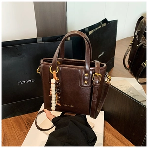 Detailed close-up of dark brown bucket bag with gold logo and beaded charm accessory