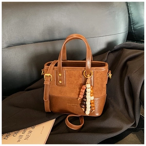 Détail d'un sac seau en cuir marron avec breloque en perles de bois sur canapé