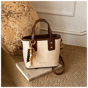 Close-up of contrast bucket bag with colorful wooden bead charm and gold hardware