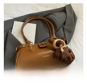 Primer plano del bolso de hombro de cuero marrón retro con un dije de oso de peluche