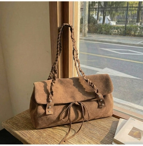 Detail of a brown suede tote bag with woven shoulder strap and decorative front bow knot