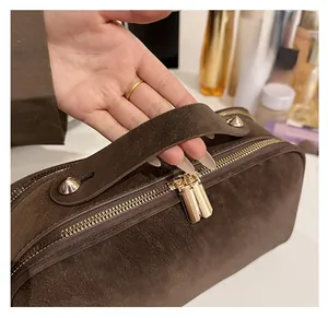 Detail der dunkelbraunen Wildleder-Kulturtasche mit bequemem Griff und goldenem Doppel-Reißverschluss