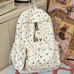 Détail du sac à dos en toile blanche avec motifs d'étoiles et porte-clé monstre peluche