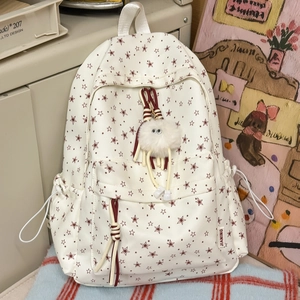 Détail du sac à dos beige à motif d'étoiles avec pendentif peluche et cordons tressés