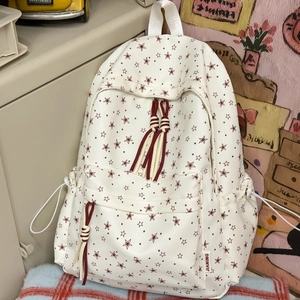 Détail d'imprimé d'étoiles rouges sur sac à dos blanc en toile avec pompon à franges