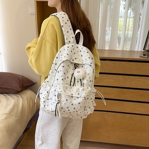 Détail du dos d'un sac à dos en toile blanche avec motifs étoiles noires et pompon
