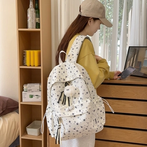 Détail du sac à dos blanc avec imprimé étoiles noires, zip avant et breloque peluche