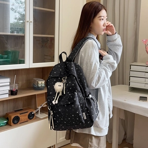 Détail du sac à dos noir en toile avec motif d'étoiles et breloque peluche blanche