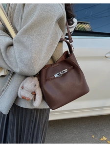 Detalle de bolso cubo en cuero marrón con cierre de giro plateado y colgante de conejo de peluche
