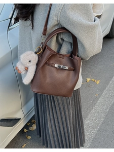 Detalle del bolso tipo cubo en cuero granulado marrón con hebilla metálica y colgante suave