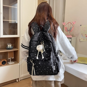 Détail du sac à dos noir avec imprimé étoiles blanches et breloque en peluche décorative