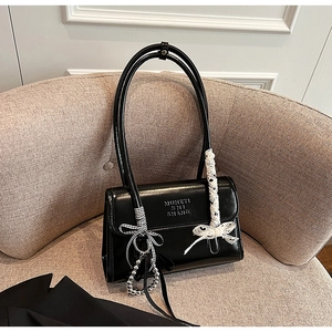 Detalle de bolso de hombro negro brillante con lazo de encaje blanco y colgantes plata