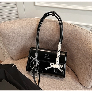 Detalle de bolso de hombro negro brillante con lazo de encaje y cinta de cuadros