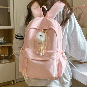 Gros plan du sac à dos rose à motif étoiles avec pendentif monstre en peluche dans un décor
