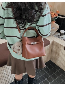 Detalle de bolso bucket de cuero granulado marrón con cierre plateado y adorno de peluche