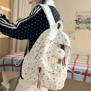 Détail d'un sac à dos en toile blanche avec étoiles rouges et porte-clé monstre peluche
