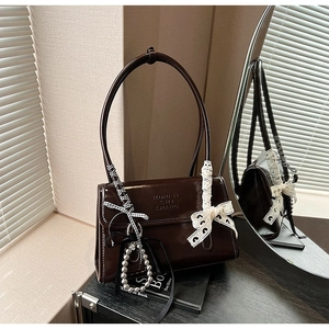 Detalle del bolso de cuero marrón oscuro con grabado de letras y cinta decorativa