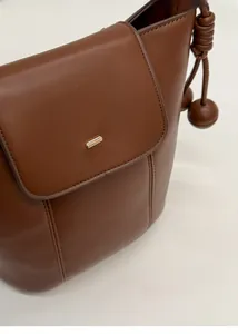 Close-up of brown leather bucket bag featuring a gold buckle and knotted side tassel