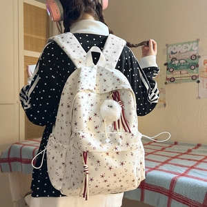 Vue détaillée d'un sac à dos blanc en toile avec des étoiles rouges et des pompons