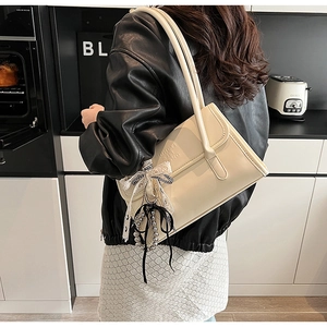 Detalle de un bolso de hombro color crema con un lazo elegante y un colgante de cuentas