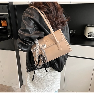 Detalle de un bolso de hombro beige brillante con lazo a cuadros y colgante de perla