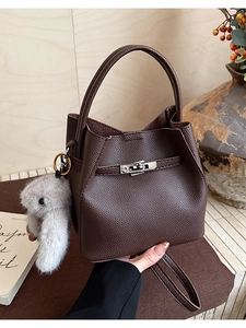 Detalle de bolso tipo cubo marrón oscuro con textura de lichi y colgante de conejo gris