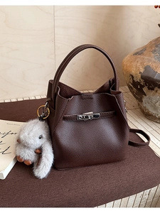 Detalle de bolso tipo cubo en cuero marrón oscuro con textura lichi, cierre y colgante