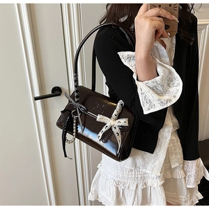 Detalle del bolso de hombro en charol marrón oscuro con lazos de encaje blanco y cadena