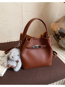 Detalle de bolso cubo en cuero granulado marrón con colgante de conejo y detalle de candado